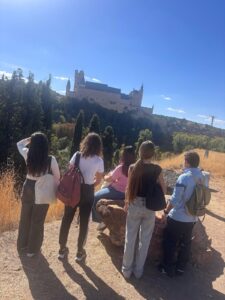 Jóvenes con mochilas contemplan un castillo sobre la ladera en día soleado