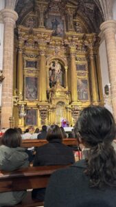 Asistentes en los bancos durante una misa ante un retablo dorado